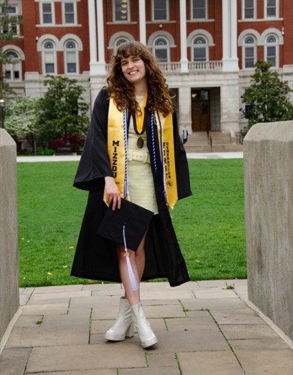 Abigail Henshaw wearing graduation regalia and posing on the Quad.