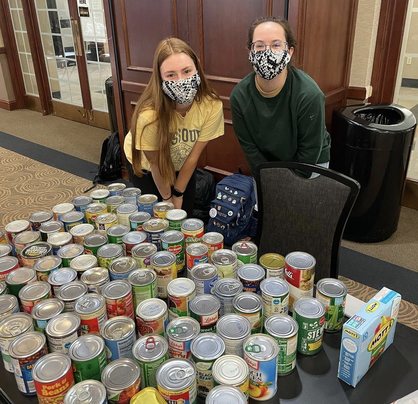 Two StuCo members smile behind a big stack of canned food.