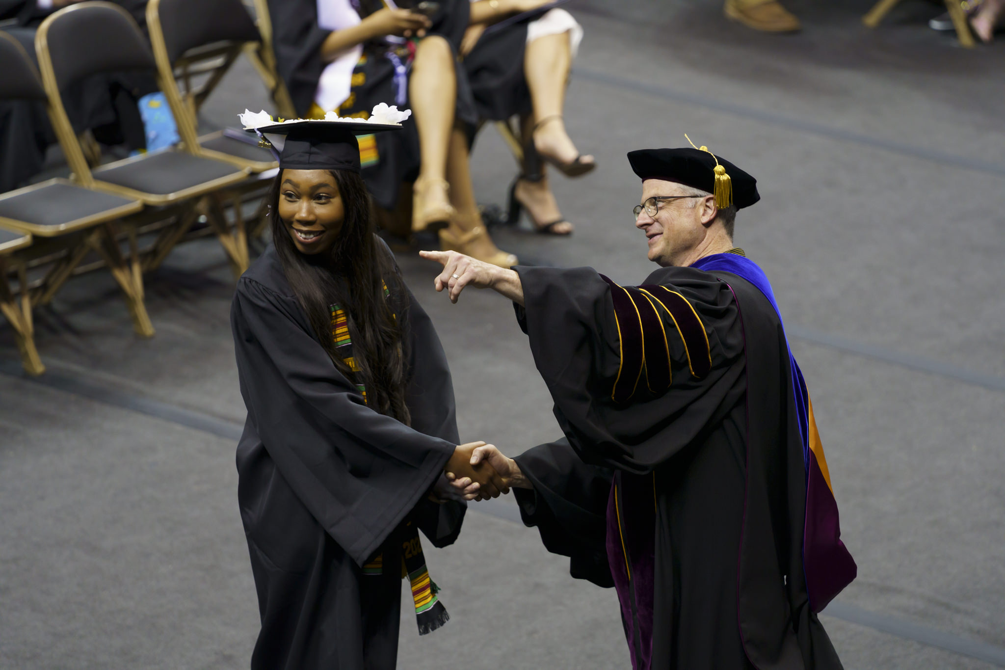 Dean Cooper Drury shaking the hand of an A&S undergraduate at commencement and pointing out someone in the crowd to her