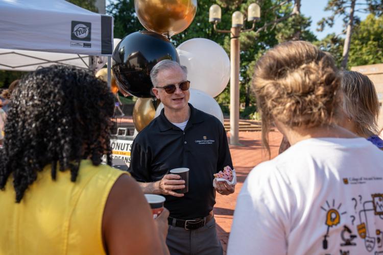 cooper drury speaks with faculty and staff while holding donut