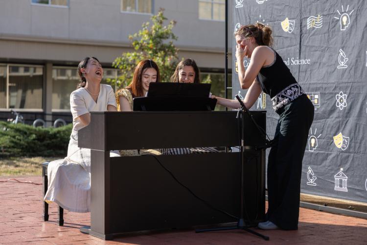 three musicians seated at piano with fourth person standing