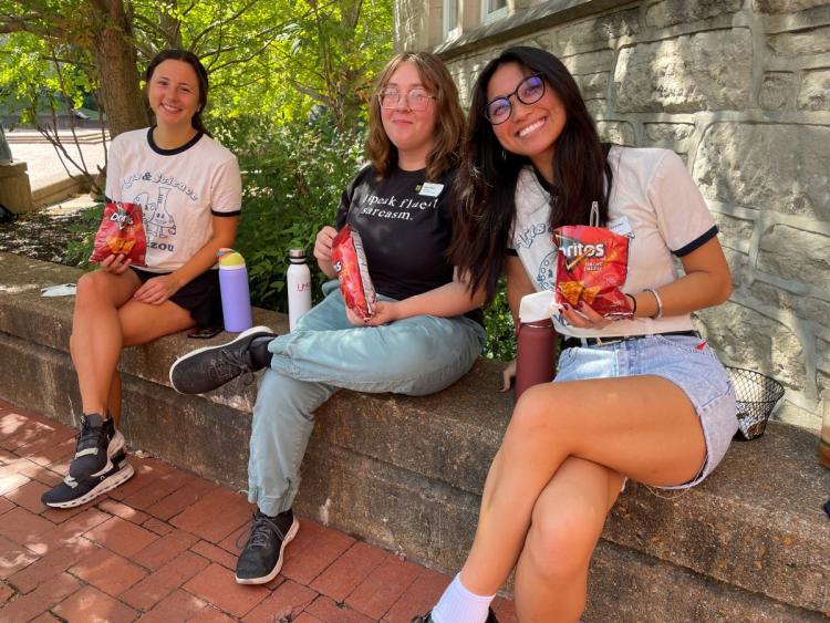 three students sitting on a low outdoor wall