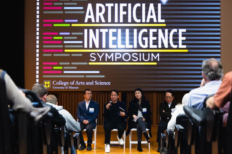 four speakers on stage at the front of an auditorium