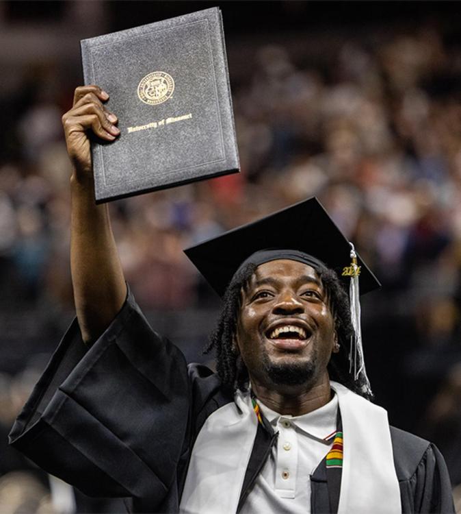 A photo of a person holding their diploma while facing the camera