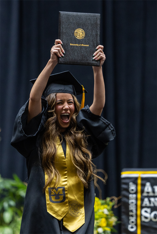 A photo of a person holding their diploma while facing the camera