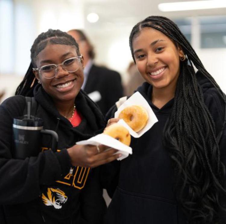 A photo of two students with donuts smiling